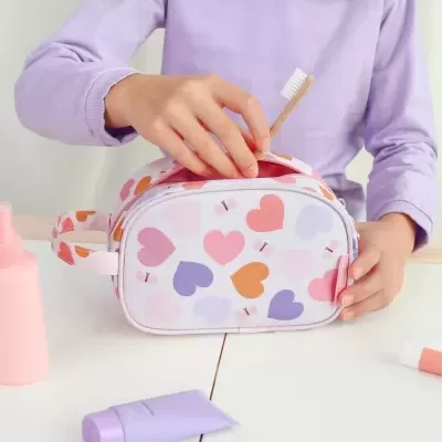 Necessaire colorida com corações, spray rosa e creme lilás num ambiente claro