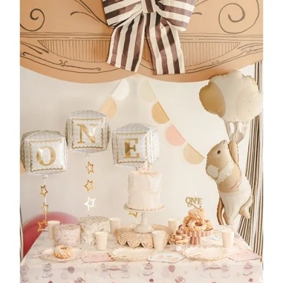 Mesa decorada de aniversário com balões brancos e dourados, bolo branco e laço riscado castanho e branco