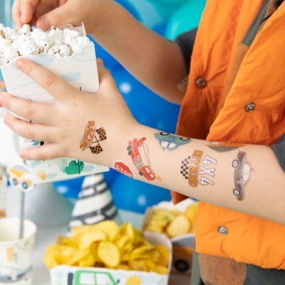 Braço de criança com tatuagens temporárias segurando caixa de pipocas