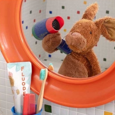 Urso de peluche no espelho com secador de cabelo e utensílios de higiene numa casa de banho.