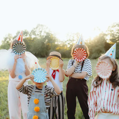 Crianças com chapéus de festa e placas listradas coloridas num campo ao ar livre