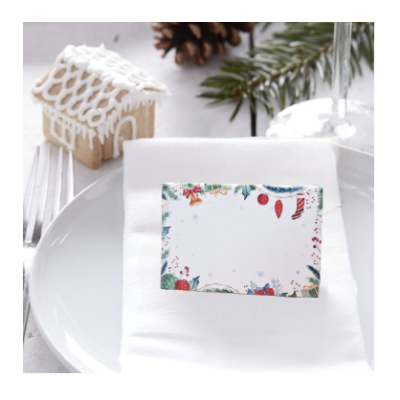 Cartão de Natal decorativo sobre guardanapo em prato, com casa de gengibre e decoração de Natal ao fundo