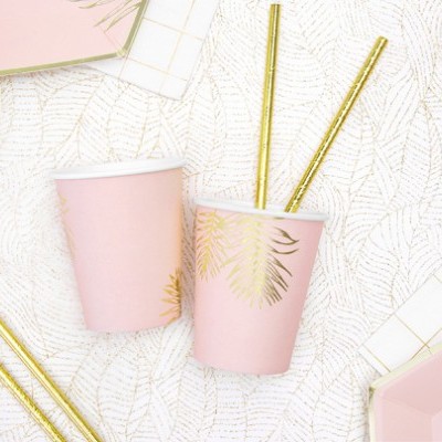 Copos de papel rosa com folhas douradas, canudos dourados, guardanapo e prato em padrão branco e dourado.