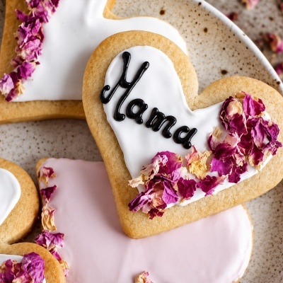 Biscoito em forma de coração decorado com glacê branco, texto e pétalas de flores secas