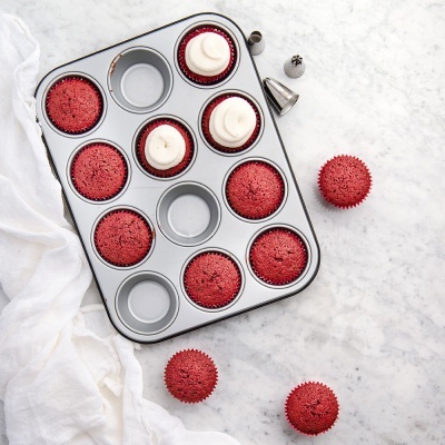 Forma metálica de cupcakes com cupcakes vermelhos e cobertura branca sobre mármore branco