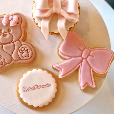 Bolachas decorativas cor-de-rosa e branco, incluindo ursinho, laço, bolacha com texto e cupcake com laço.