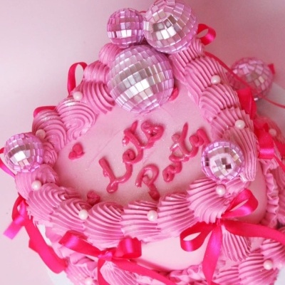 Bolo decorado rosa com chantilly, laços, bolinhas brancas e bolas prateadas, texto Lets Party.