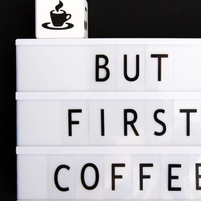 Placa luminosa com texto 'BUT FIRST COFFEE' e cubo com chávena de café