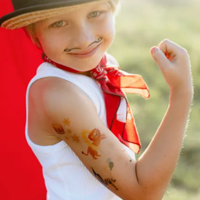 Criança com tatuagens temporárias e chapéu de palha a sorrir e mostrar o braço