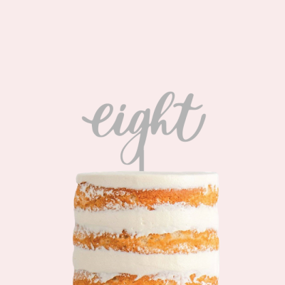 Bolo de camadas bege e branco com topper 'eight' cinzento sobre fundo cor-de-rosa