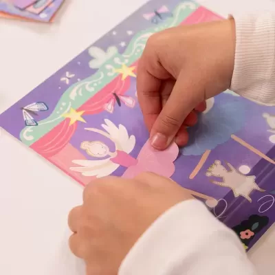 Livro ou atividade de paper craft com ilustrações coloridas e peça cor-de-rosa sendo colocada por mãos de criança