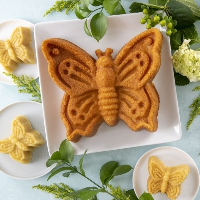 Bolo em forma de borboleta num prato branco com bolos menores e decorações florais