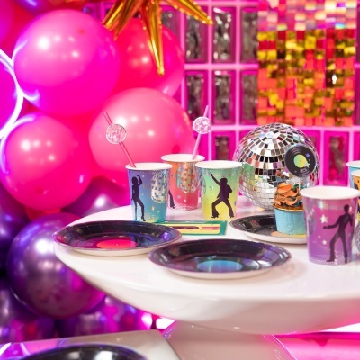 Mesa com copos descartáveis de dança disco, pratos pretos, cupcake colorido e globo discoteca prateado