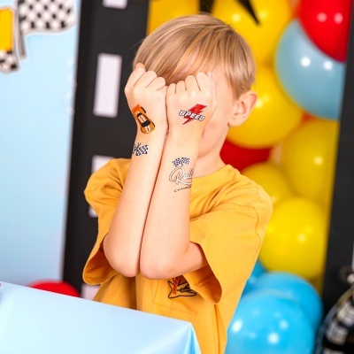 Criança com tatuagens temporárias de corrida nas mãos, camiseta amarelo mostarda e balões ao fundo