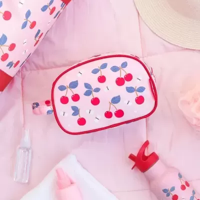 Bolsa rosa com padrão de cerejas vermelhas sobre tapete rosa com acessórios