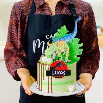 Bolo decorado com dinossauros e texto 'LUCAS' numa base branca