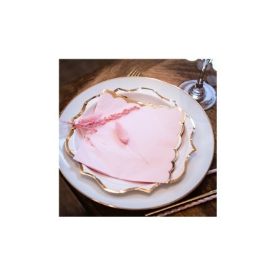 Conjunto de pratos brancos com bordas douradas, guardanapos rosa e ramo rosa seco numa mesa de madeira