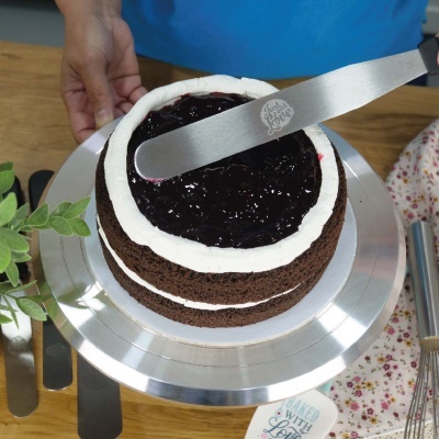 Bolo de chocolate com creme branco e geleia negra sendo espalhada com espátula 'Bake with Love'