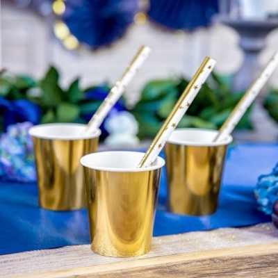 Três copos dourados com canudos brancos decorados numa mesa com decoração azul e uvas.