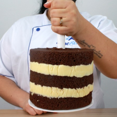 Bolo de chocolate com creme amarelo em camadas segurado por pessoa com uniforme branco e azul