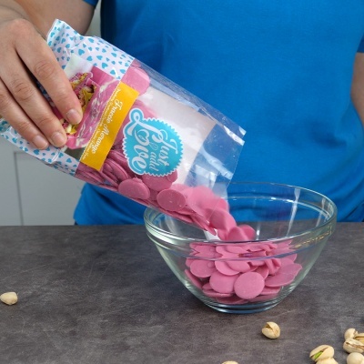 Pacote plástico aberto com gotas rosa 'Yummy Candy' a cair em taça de vidro na mesa.