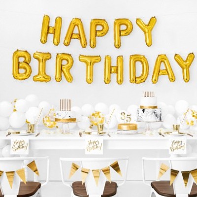 Decoração de festa com balões dourados HAPPY BIRTHDAY e bolos numa mesa com decorações branco e dourado