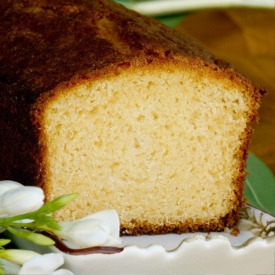 Fatia de bolo amarelo húmido num prato branco com flores brancas