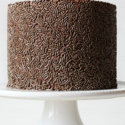 Bolo alto coberto de chocolate com granulado de chocolate em prato branco