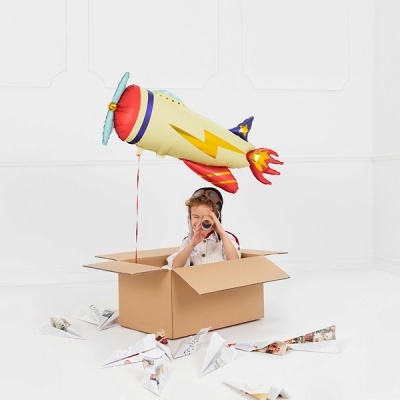 Criança dentro de caixa de cartão com balão de foguete e aviões de papel