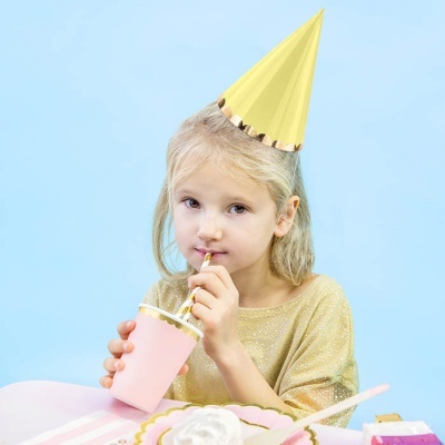 Menina loira com chapéu de festa amarelo a beber de copo rosa com canudo, fundo azul