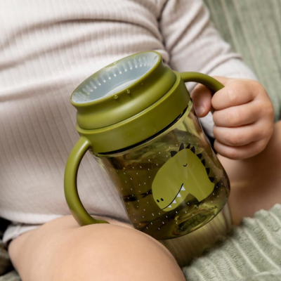 Copo infantil verde com desenho de dinossauro e tampa cinza segurado por criança