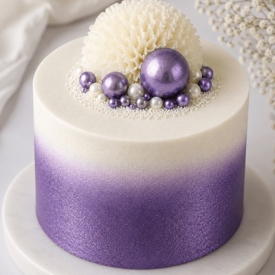 Bolo redondo branco e roxo decorado com bolas e flor no topo sobre suporte de mármore