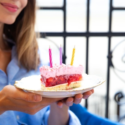 Fatia de bolo de morango com velas coloridas num prato branco com borda dourada