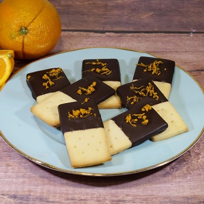 Bolachas retangulares meio mergulhadas em chocolate e decoradas com raspas de laranja num prato azul