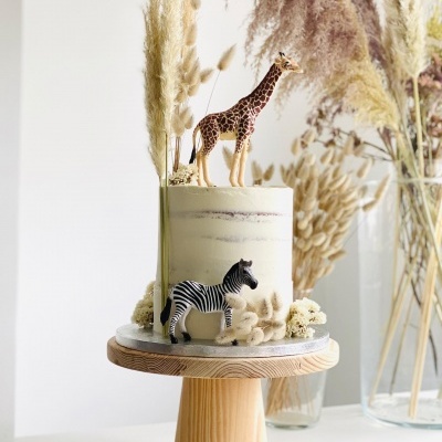 Bolo decorado com figuras de girafa e zebra e flores secas sobre suporte de madeira