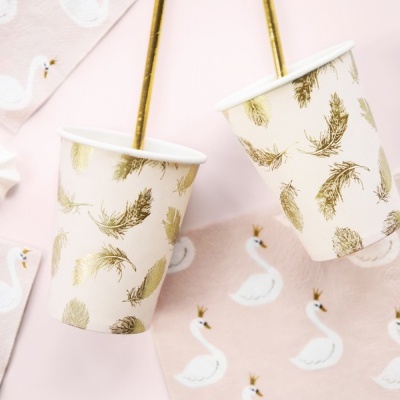 Copos de papel com padrão dourado e guardanapos com cisnes em fundo rosa