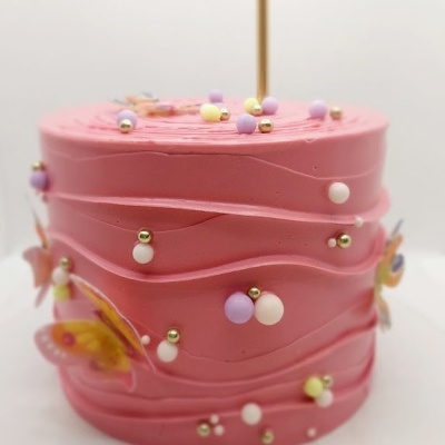 Bolo rosa com decoração colorida, borboletas e vela dourada