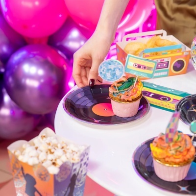 Cupcakes coloridos com cobertura e toppers de disco espelhado e cassete em pratos de disco de vinil em festa colorida com balões e snacks