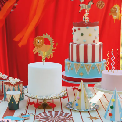 Bolos e cupcakes decorados com tema de circo em várias cores e padrões sobre mesa com fundo vermelho