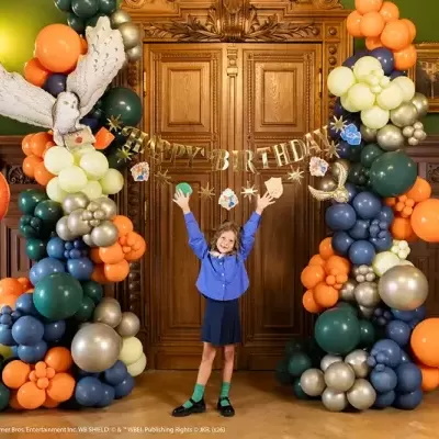 Arco de balões coloridos com decoração Harry Potter e menina em frente a porta de madeira