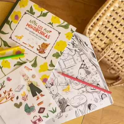 Livro de colorir LES MINOUCHIKAS com desenhos e adesivos sobre mesa de madeira