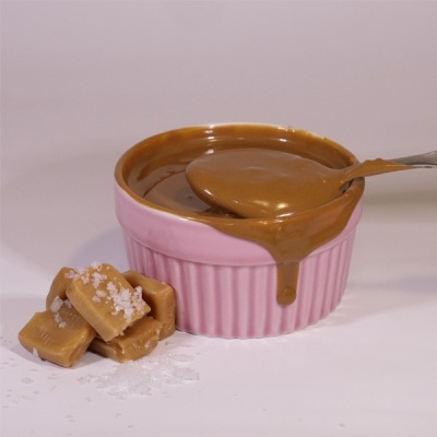 Taça rosa com molho castanho e colher, caramelos salgados ao lado em superfície branca