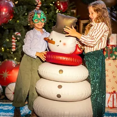 Crianças com boneco de neve insuflável em ambiente natalício decorado.