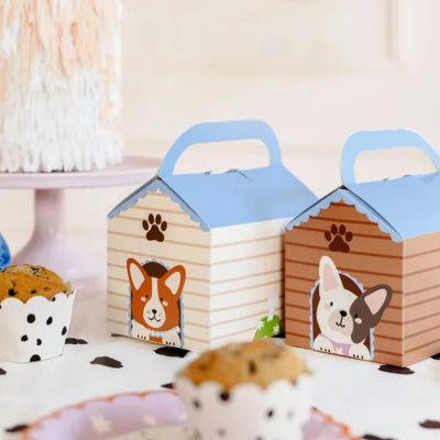 Caixas de presente em forma de casinha com imagem de cães e muffins numa mesa branca decorada