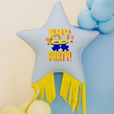 Balão metálico em forma de estrela cinzenta com desenhos e texto, com balões azuis e amarelos ao redor
