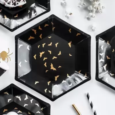 Pratos hexagonais pretos decorados com morcegos dourados e aranhas prateadas com donuts e pipocas