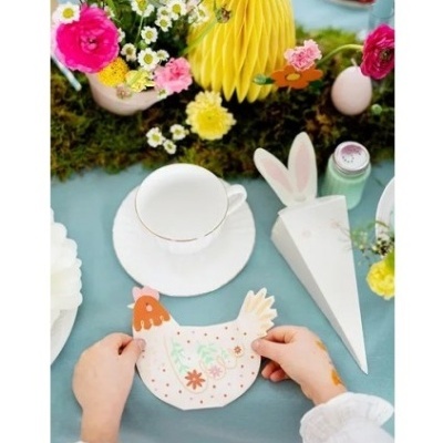 Mesa decorada com flores coloridas, suporte amarelo de papel em forma de abelha, xícara branca, recipiente com orelhas de coelho e cartão em forma de galinha