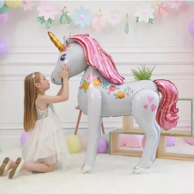 Balão metalizado de unicórnio com crina rosa e criança ao lado numa decoração com flores e balões