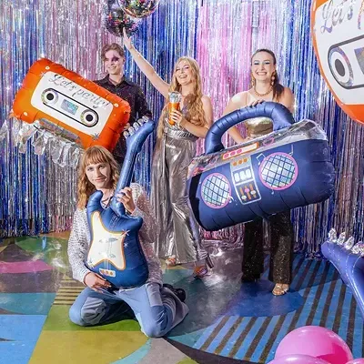 Pessoas numa festa com objetos insufláveis temáticos de música e decoração prateada