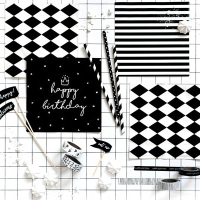 Artigos de festa preto e branco com padrões geométricos e texto 'happy birthday' numa superfície quadriculada